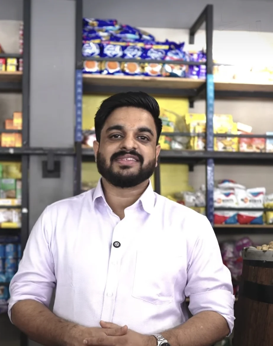 Akshay Murali in the Murali Brand store in Calicut, shelves of spices, rice and groceries behind him